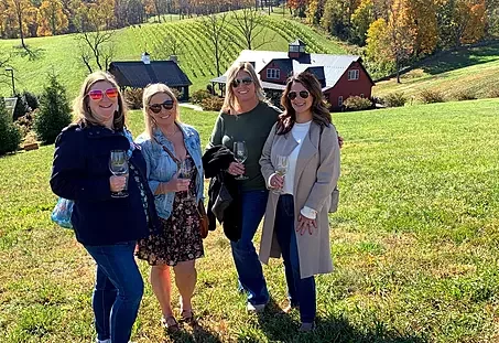 A group of friends enjoys a sunny afternoon at Williams Gap Winery in Loudoun County, Virginia, with vineyards in the background.
